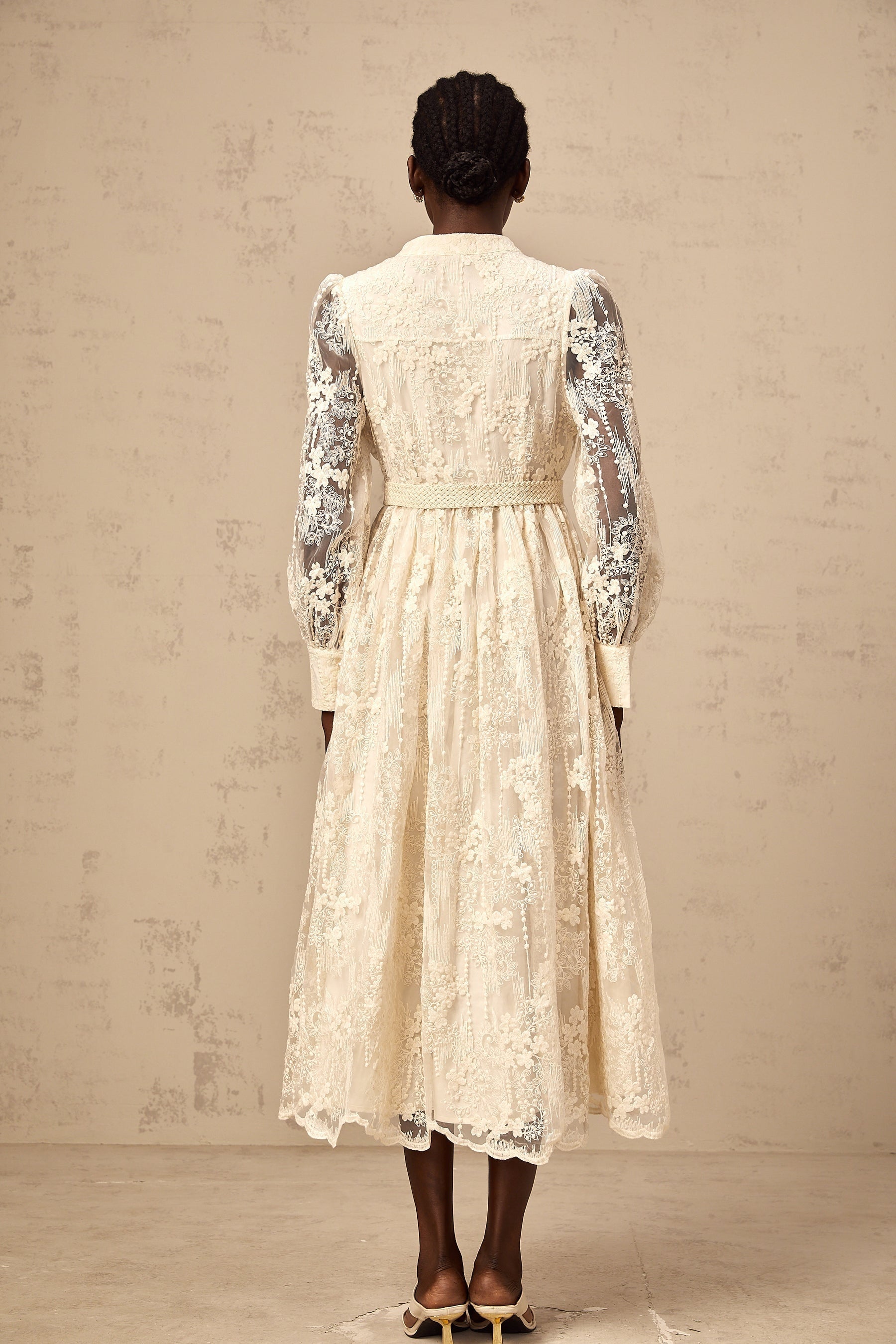 Woman wearing a neutral colored midi dress with lace embroidery details and a flowy silhouette