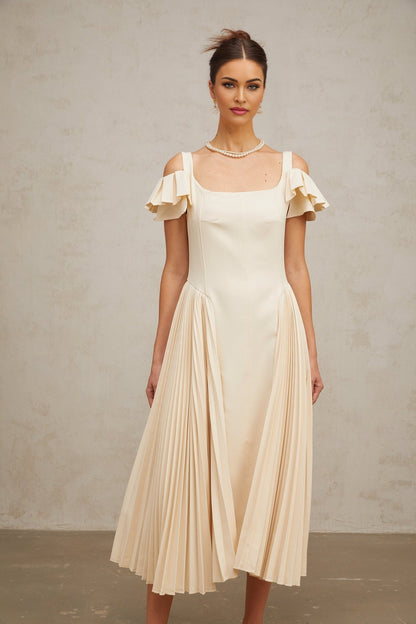 Woman wearing neutral colored pleated flared midi dress with long sleeves and V neckline