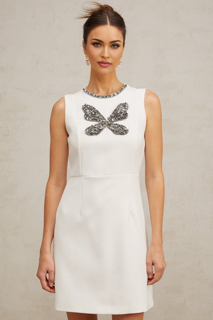 A white mini dress with crystal butterfly embellishments on a model against a plain background