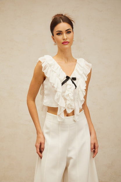 A white cropped top made of chiffon fabric featuring a bow knot detail and ruffled trim