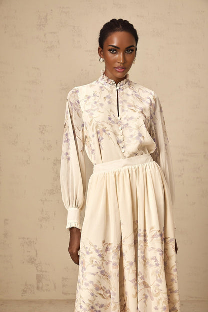 Woman wearing a matching shirt and skirt set with frilled details and wisteria floral print in light colors