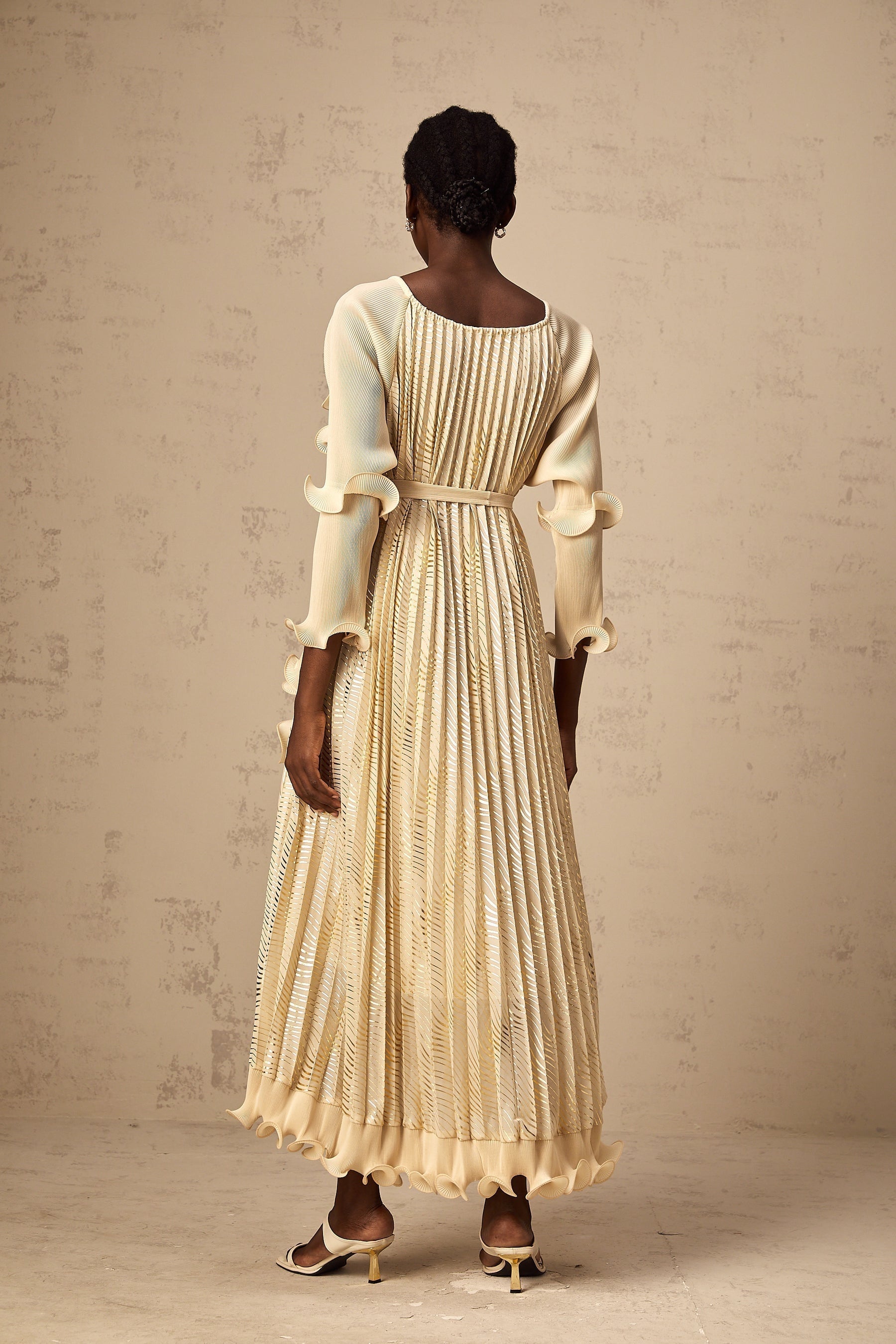 A woman wearing a neutralcolored midi dress with gilded ruffles and delicate details standing in a relaxed pose