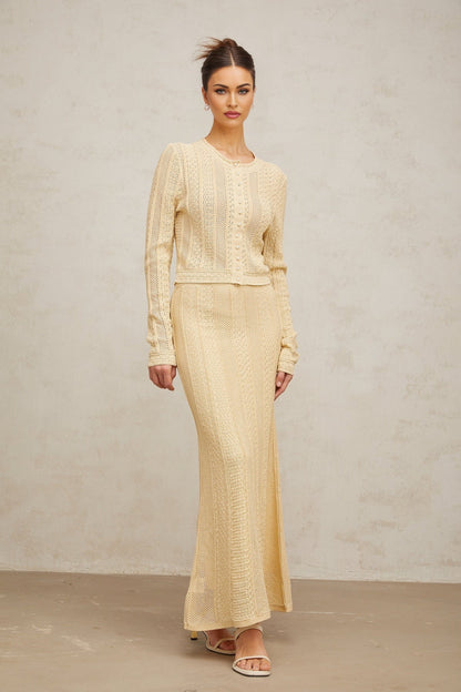 Matching set of a pointelle knit cardigan and skirt in light color worn by a model against a plain background