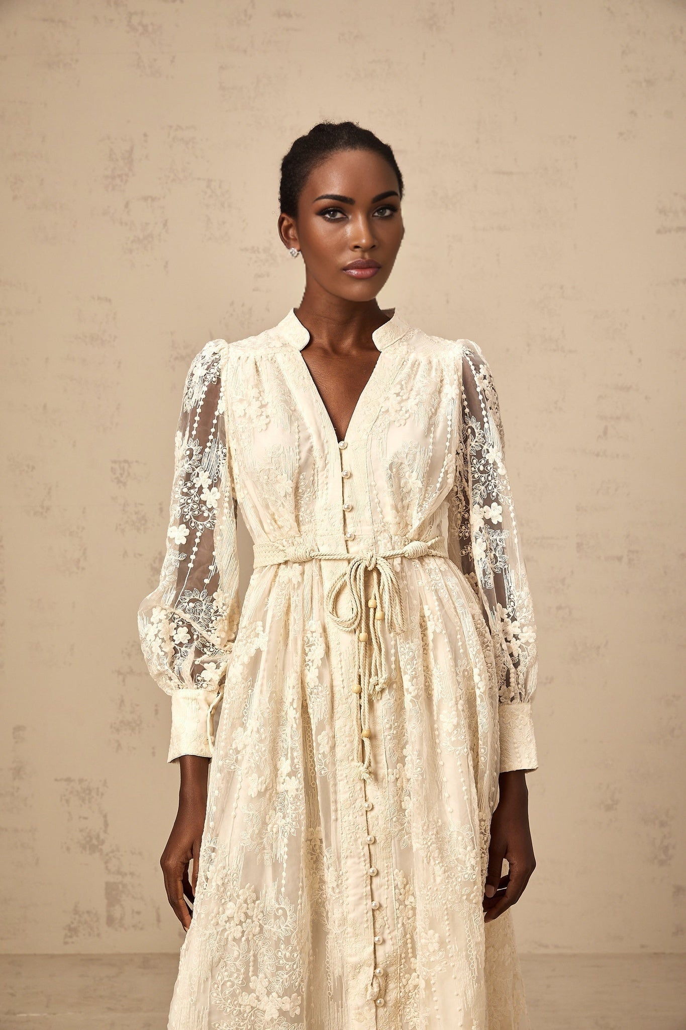 Woman wearing beige lace embroidered midi dress with intricate floral patterns standing in neutral background
