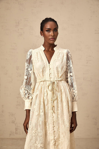 Woman wearing beige lace embroidered midi dress with intricate floral patterns standing in neutral background