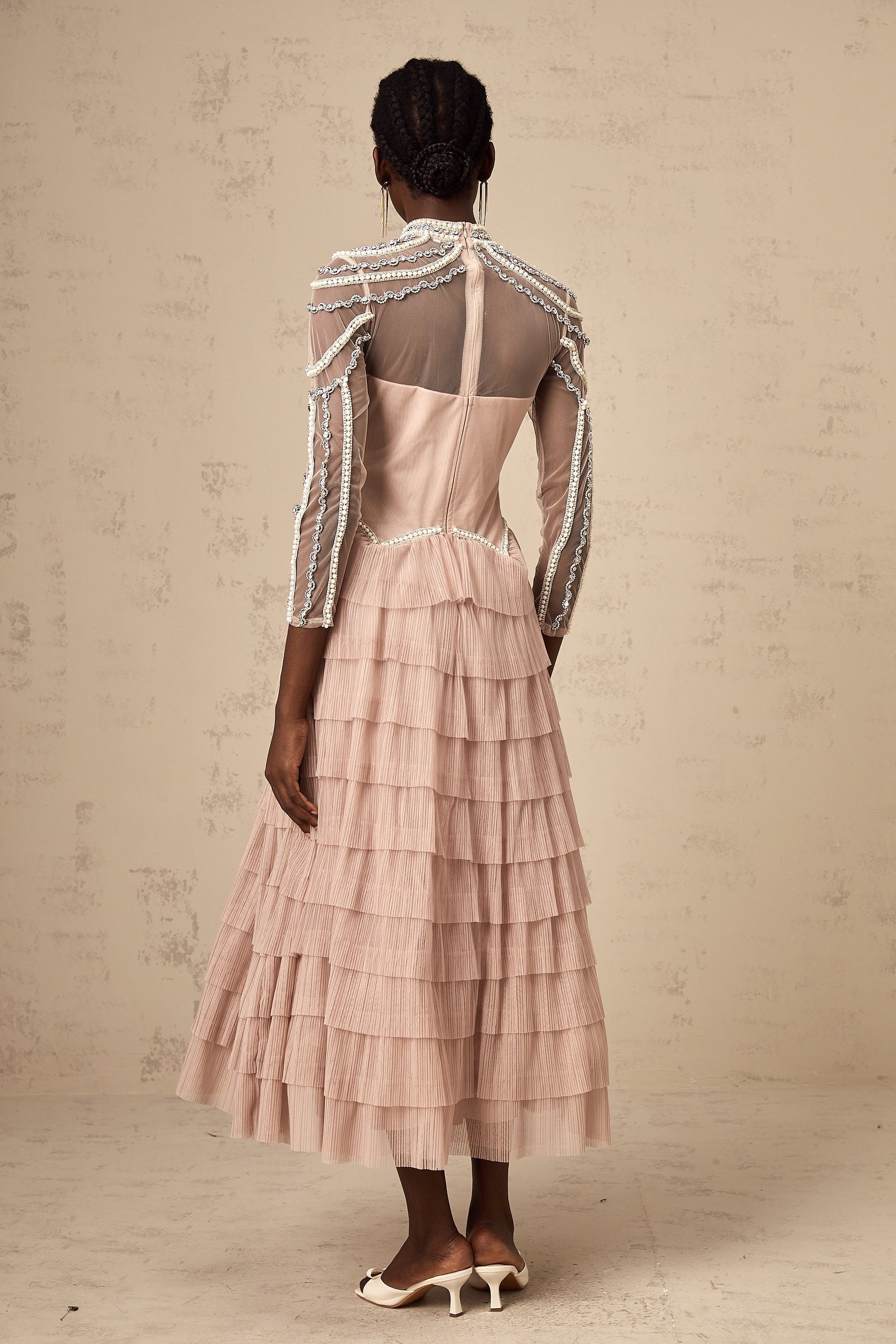 A pink beaded gown with tiered layers and semi sheer fabric featuring a long flowing silhouette