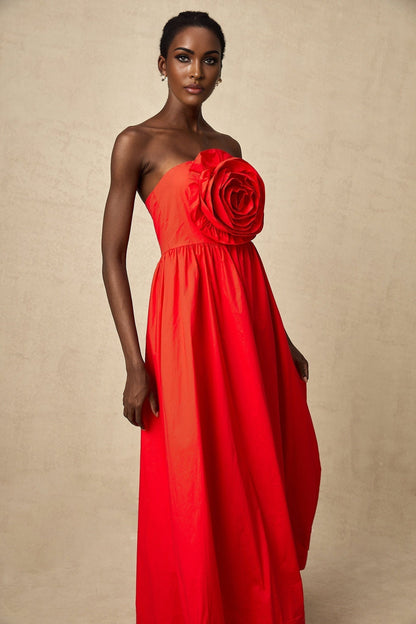 A woman wearing a long red maxi dress with cascading 3d floral petal ruffles covering the bodice and skirt