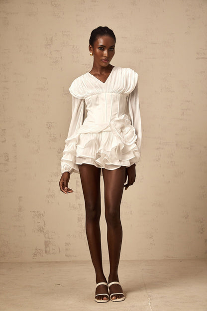 A white mini dress with full pleats and a cinched waist on a model against a plain background
