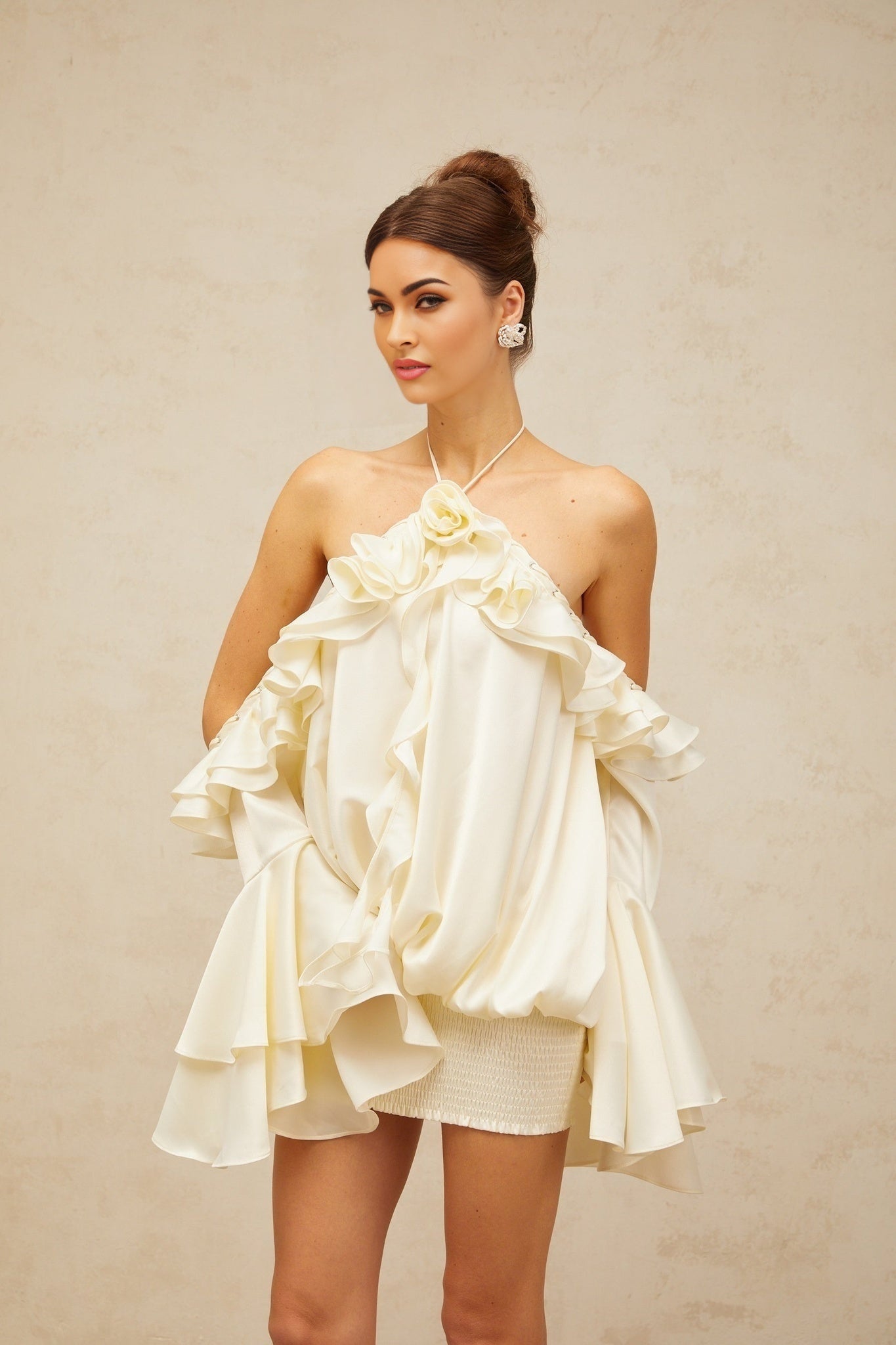 A woman wearing a short floral print dress with ruffled details and exposed shoulders standing against a plain background