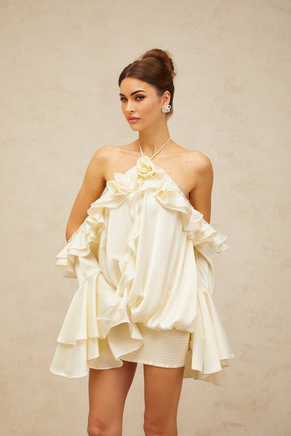 A woman wearing a short floral print dress with ruffled details and exposed shoulders standing against a plain background