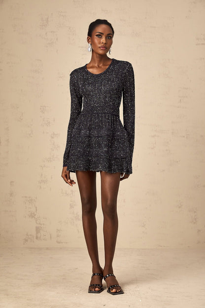 Woman wearing a short black knitted dress with sequin embellishments form fitting silhouette and mini length