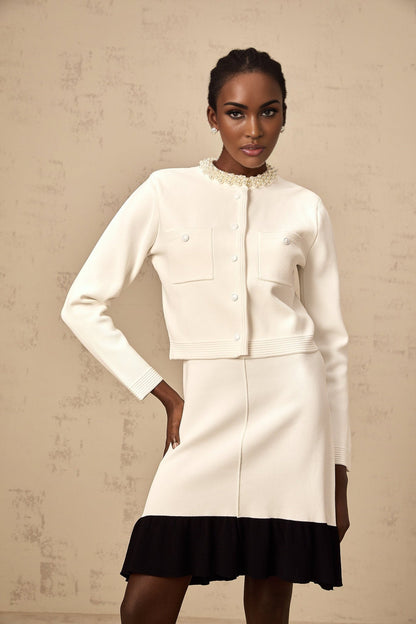 A white knitted cardigan with faux pearl embellishments worn by a model against a plain background