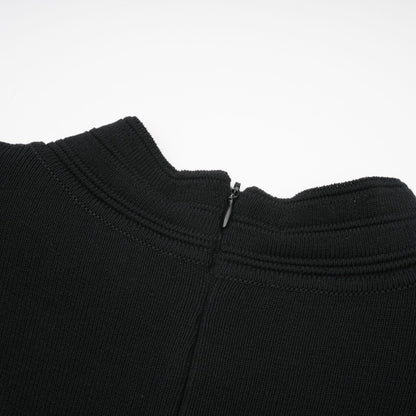 A black knitted mini dress with ruffled details and embellishments worn by a model standing against a plain background