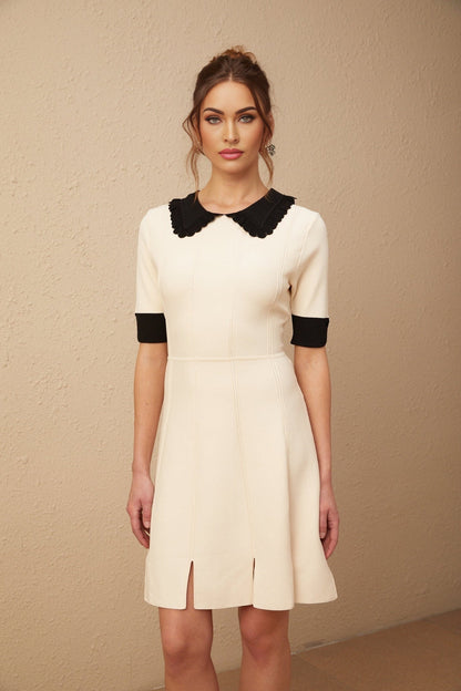 Young woman wearing a white knitted mini dress with split hem detail standing in front of plain background