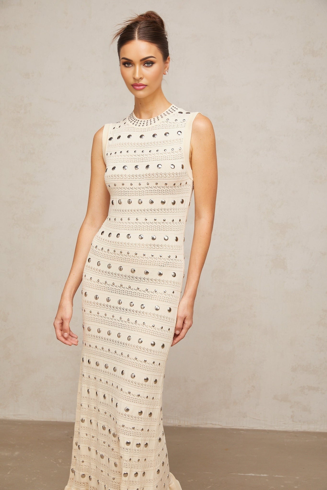 A long neutralcolored maxi dress with crochetknit pattern and studded details made by Chloé