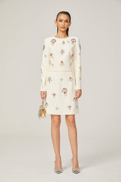 A woman wearing a white matching set consisting of a sleeveless top and skirt adorned with crystal embellishments