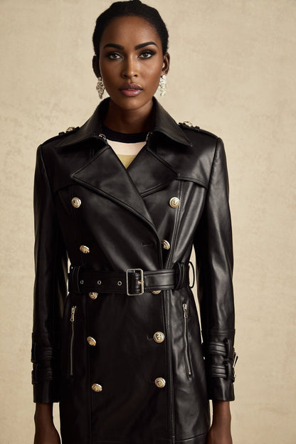 A woman wearing a black leather coat with doublebreasted front buttons and a belt at the waist The coat is long and has a classic style
