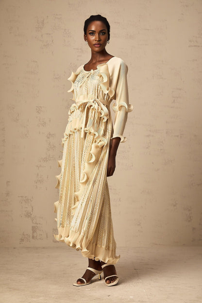 A woman wearing a neutralcolored midi dress with gilded ruffles and a fitted silhouette standing in a relaxed pose