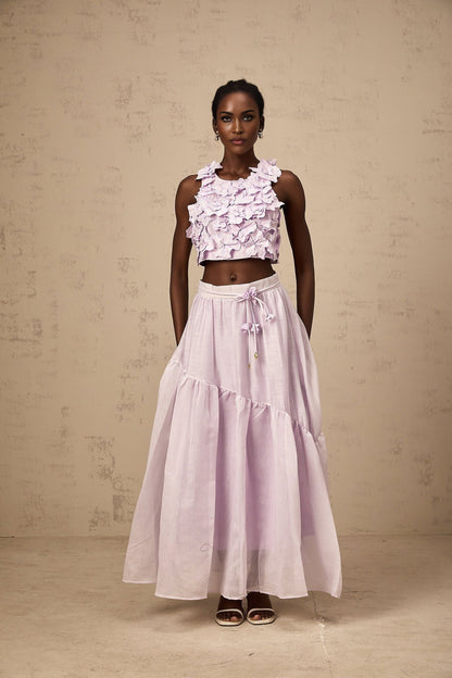 Woman wearing purple two piece outfit consisting of floral top and matching skirt with faux flower design
