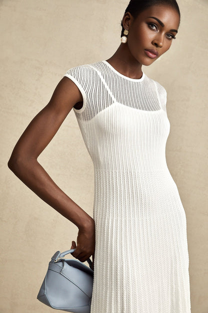 A white semisheer midi dress with scalloped hem details named Liane worn by a model standing against a plain background