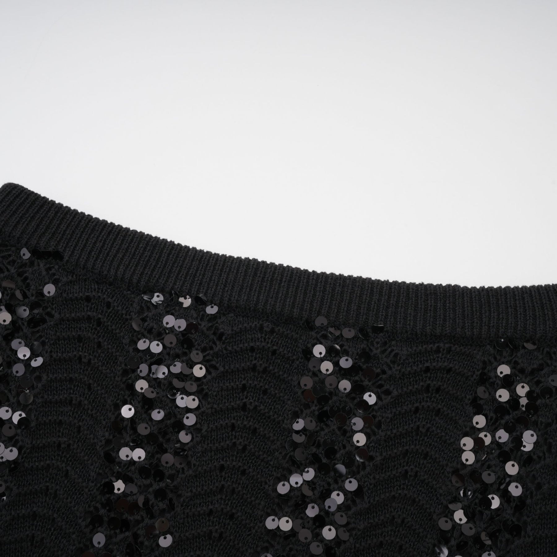 Woman wearing black sequined crochet knit cardigan and matching skirt set