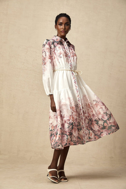 A woman wearing a floral print midi dress with lantern sleeves standing in a casual pose against a plain background