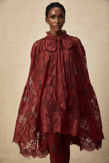A woman wearing a vibrant red oversize dress made of delicate chantilly lace standing in a relaxed pose against a plain background