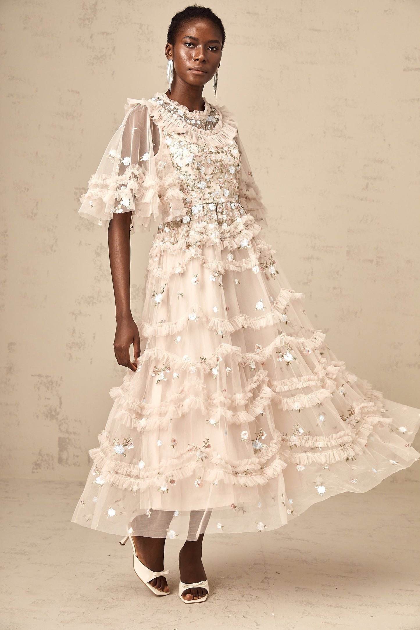 A woman wearing a midi length dress with tiered ruffles and floral embroidery design standing in a relaxed pose
