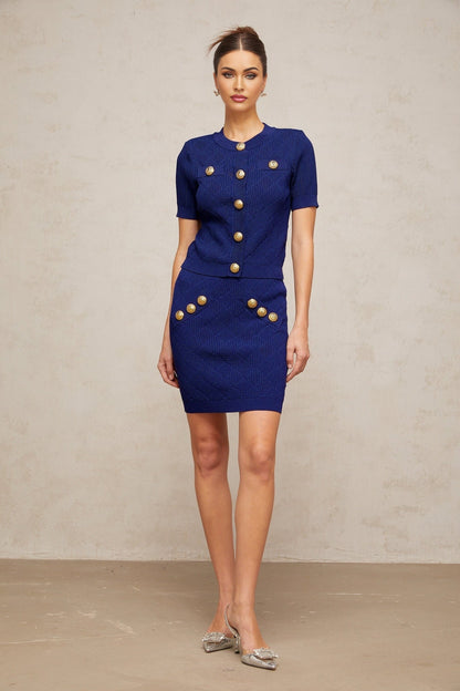 A blue plaid knit top and matching skirt set featuring a checkered pattern throughout Both pieces are coordinated in style and color creating a cohesive outfit The top is likely short sleeved or sleeveless while the skirt appears to be knee length or above