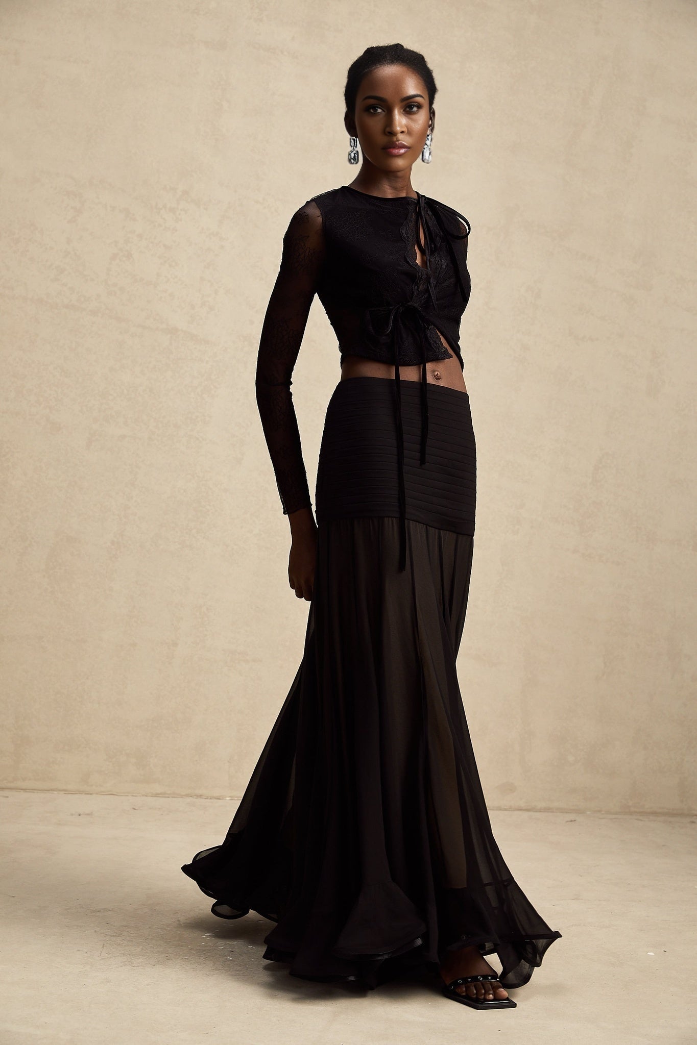 A black sheer cropped top with lace trim details worn by a model against a plain background