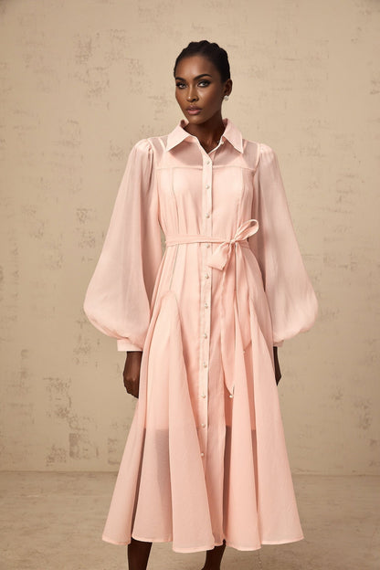 Woman wearing a pink midi length shirt dress with a tied waist detail and collar