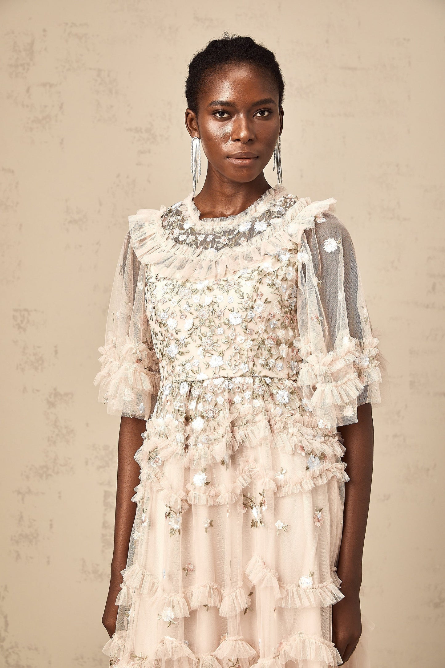 A white midi dress with tiered ruffles and delicate floral embroidery details throughout featuring a feminine silhouette and sleeveless design