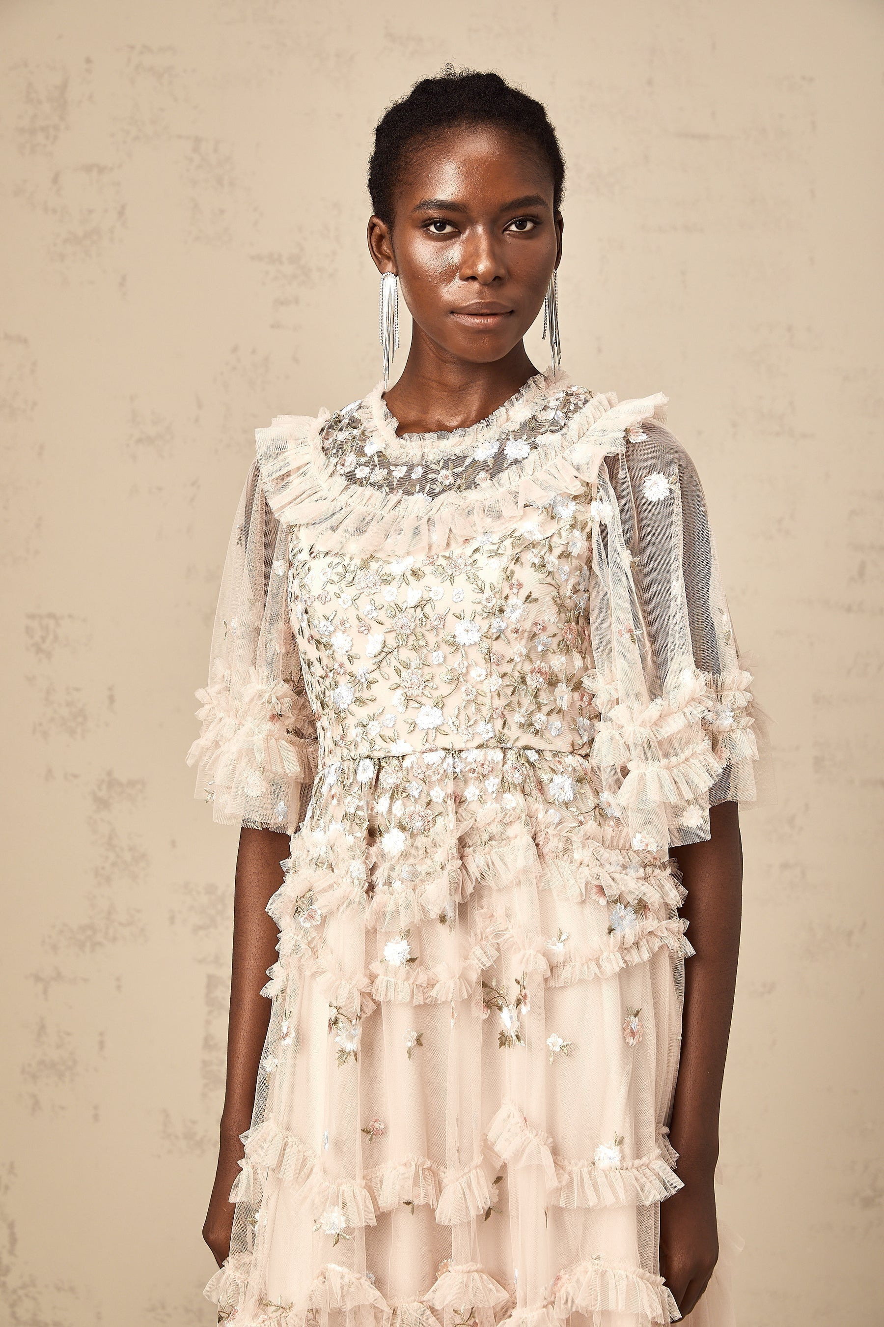 A white midi dress with tiered ruffles and delicate floral embroidery details throughout featuring a feminine silhouette and sleeveless design