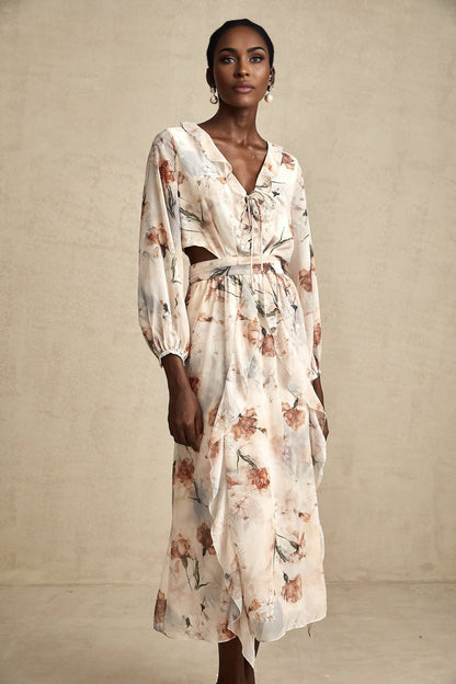 A woman wearing a floral print midi dress with an open waist design The dress features a colorful pattern on a light background and has a flowing silhouette that falls to mid calf length