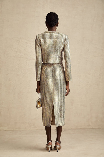 A woman wearing a gold tweed jacket and matching skirt set adorned with sequins The outfit has a luxurious and sparkling appearance suitable for formal or evening events