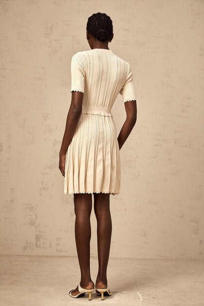 A lightcolored mini dress with a pleated knit design and delicate pointelle trim details along the edges