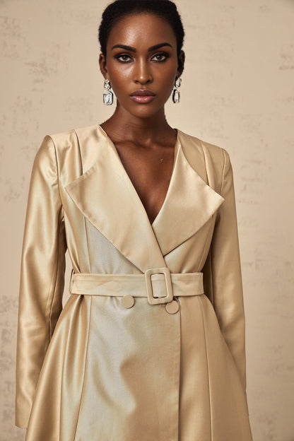 Woman wearing long khaki coat with belt at waist standing in urban setting