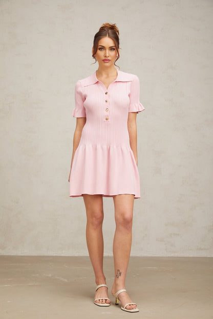 Young woman wearing a pink flared mini dress with fine knit fabric standing against a plain background