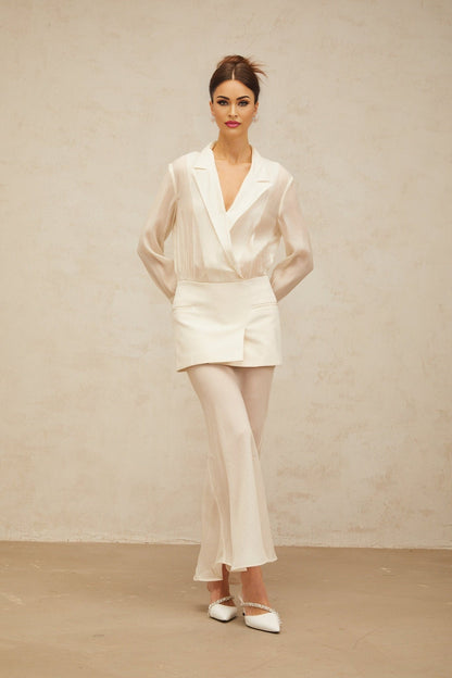 A woman wearing a long flowing white maxi dress with sheer panels standing in a relaxed pose