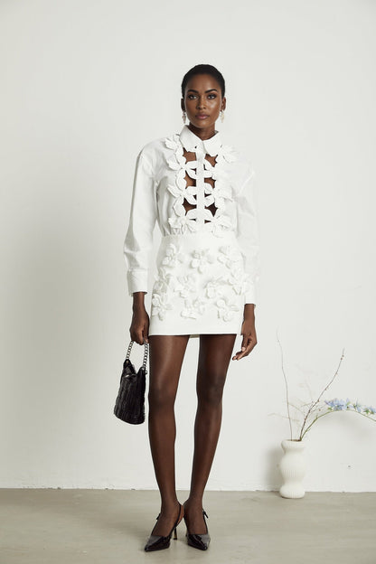A white buttonup shirt with floral cutout patterns and short sleeves featuring a collar and relaxed fit