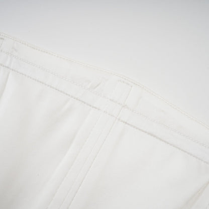 A woman wearing a long white pleated maxi dress with an offshoulder neckline