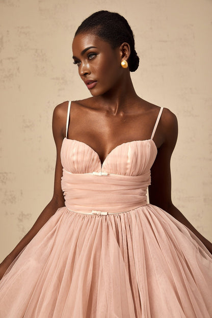 Young woman wearing a sleeveless white tulle mini dress with pleated details and a fitted bodice standing against a plain background