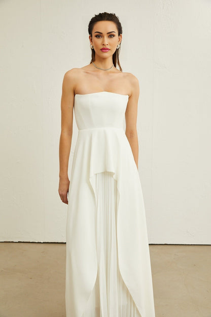 Woman wearing a white pleated off shoulder maxi dress standing in a neutral background