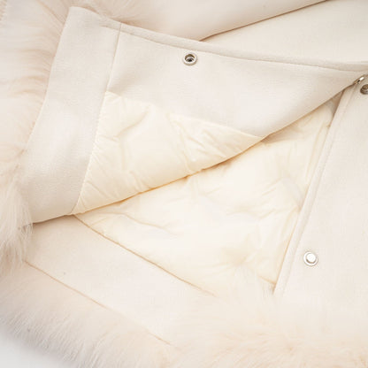 Woman wearing white suede short coat with fur trim and padded design standing against plain background