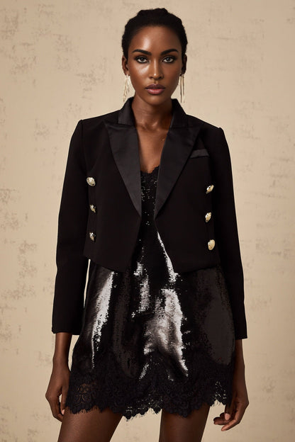 A black cropped blazer with double breasted buttons worn by a model against a plain background