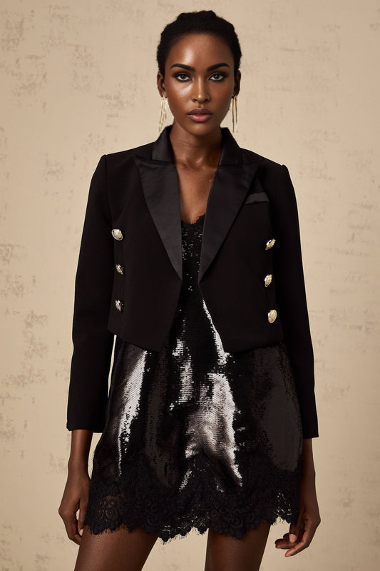 A black cropped blazer with double breasted buttons worn by a model against a plain background