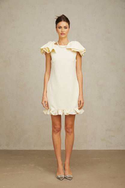 Young woman wearing a short white mini dress with ruffled details and a bow accent standing in a casual pose