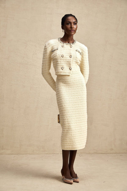 A woman wearing a matching knit cardigan and skirt set with embellishments The cardigan is open in the front and the skirt falls to about knee length The set is likely in a light color with decorative details