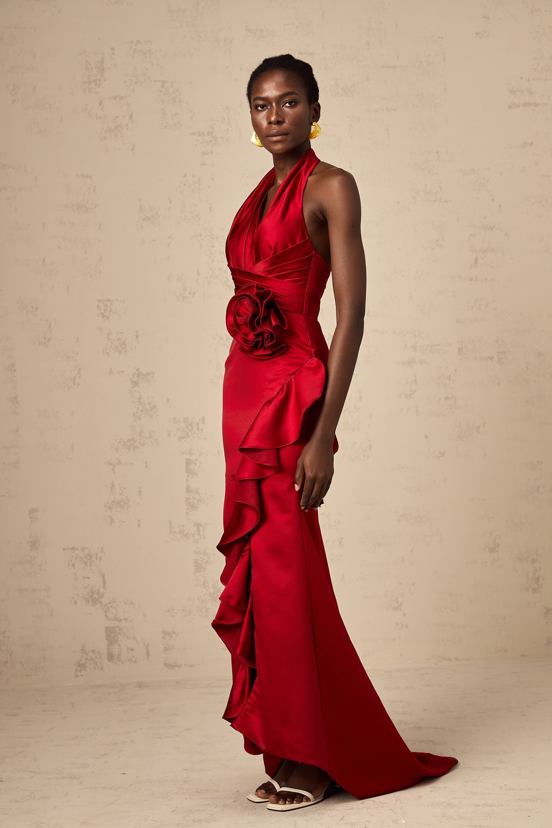 A vibrant red halterneck maxi dress with cascading 3D petal ruffles along the skirt featuring a fitted bodice and floor length design