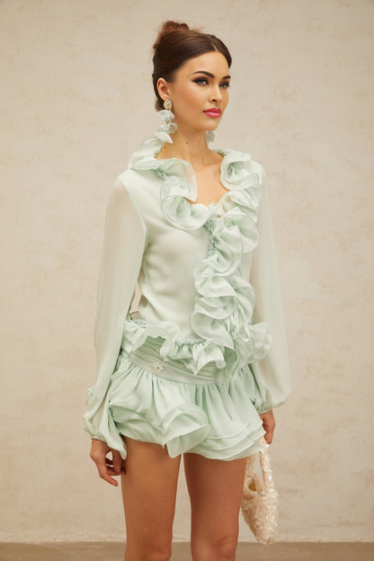 A woman wearing a matching green chiffon outfit consisting of a flounced blouse and skirt set by Noémie